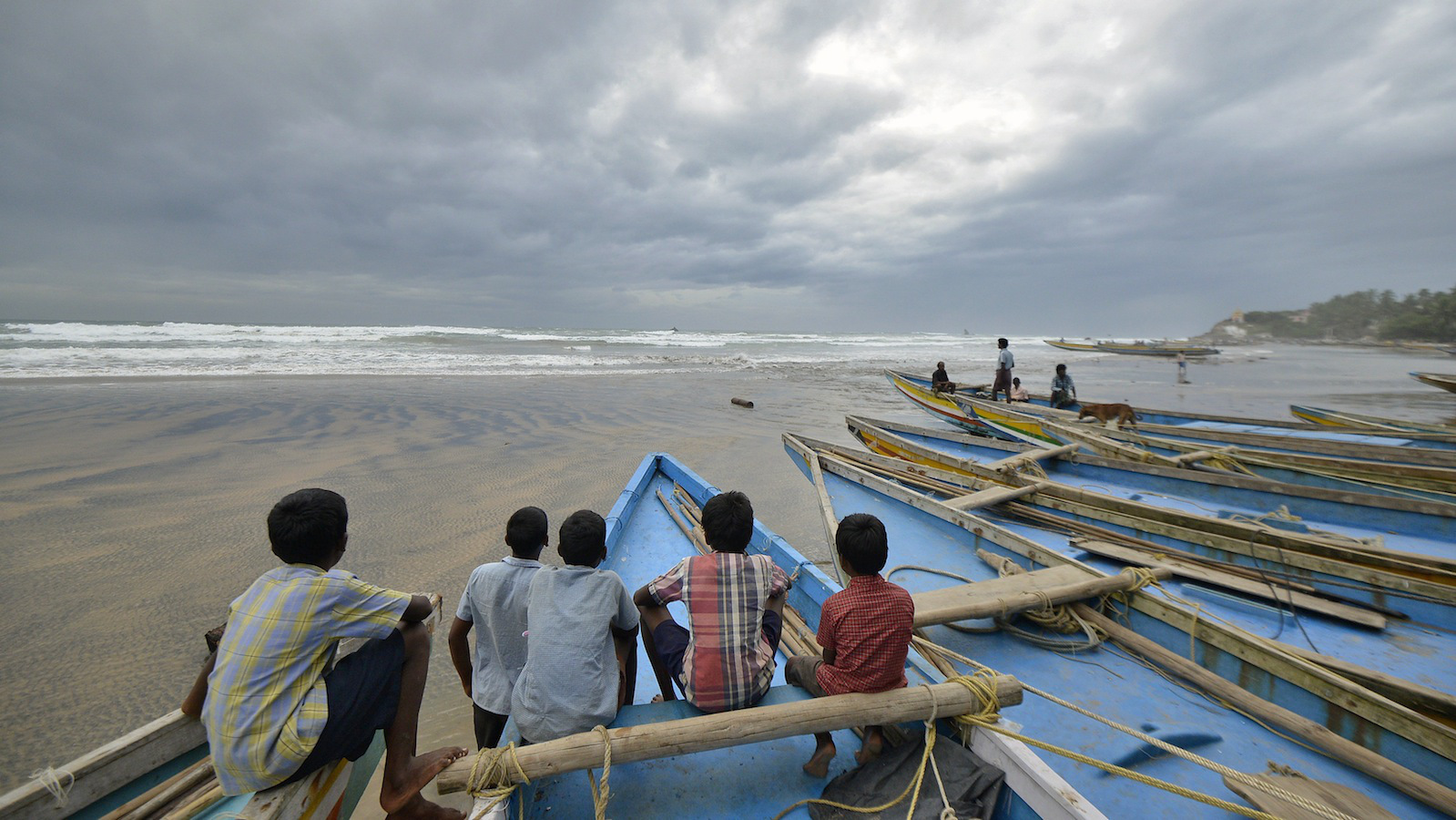 Children sit on fishing boats by the shore before being evacuated, at Visakhapatnam district