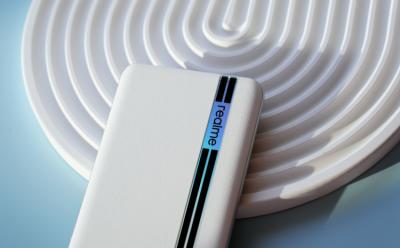 A Realme device with while leather back and the Realme logo placed half on a white circular object and a blue table