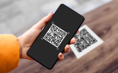 hand holding phone with a QR code on the screen over another code in the background