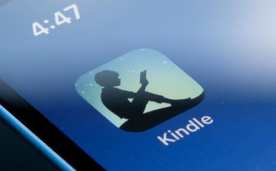 shot of the Amazon Kindle iOS app icon on an iPhone screen with a blue wallpaper