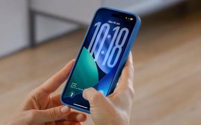 hand holding an iPhone previewing the iOS 26 lock screen in dark mode