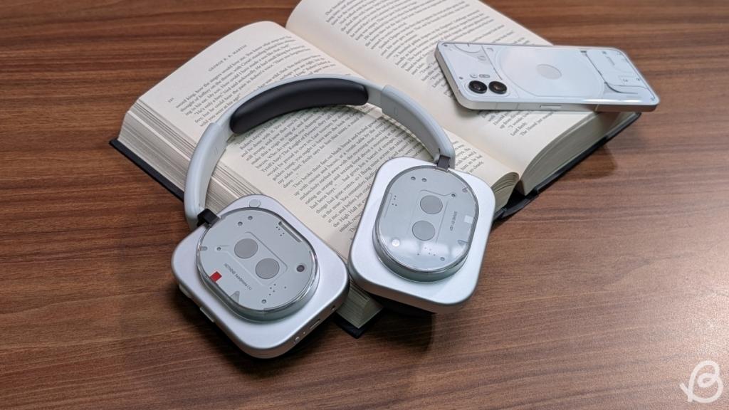 Nothing Headphone (1) lying on a book next to the Nothing Phone (2)