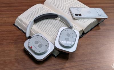 Nothing Headphone (1) lying on a book next to the Nothing Phone (2)
