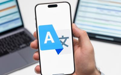 Google Translate logo on the screen of smartphone in mans hand and laptop on the background